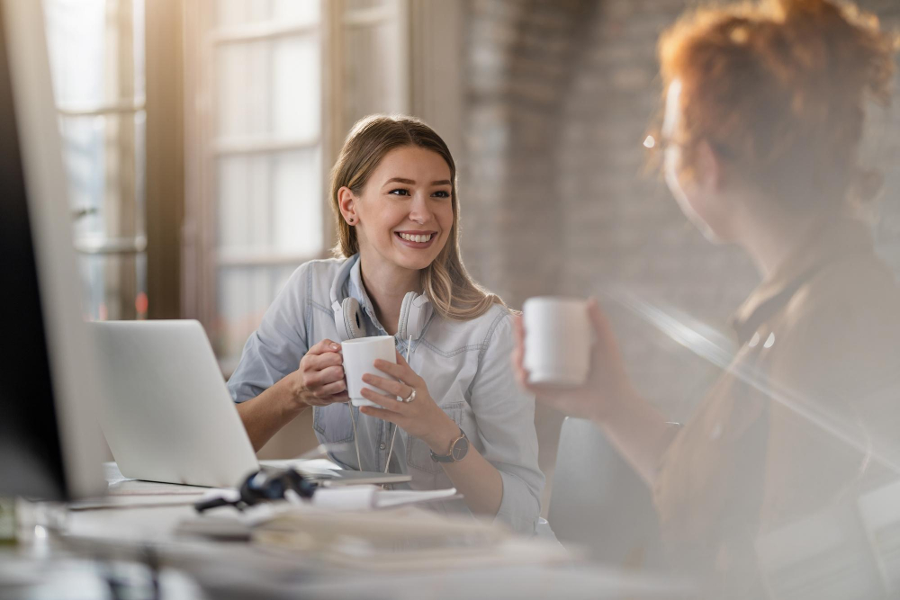 Young smiling businesswoman and her female colleague communicating while having coffee break in the office